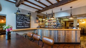 Een rustieke bar met houten balken, een krijtbordmenu en een bar vol flessen.