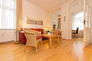 Een gezellige woonkamer met een rode bank, twee rieten fauteuils, een houten salontafel en een vloerlamp.