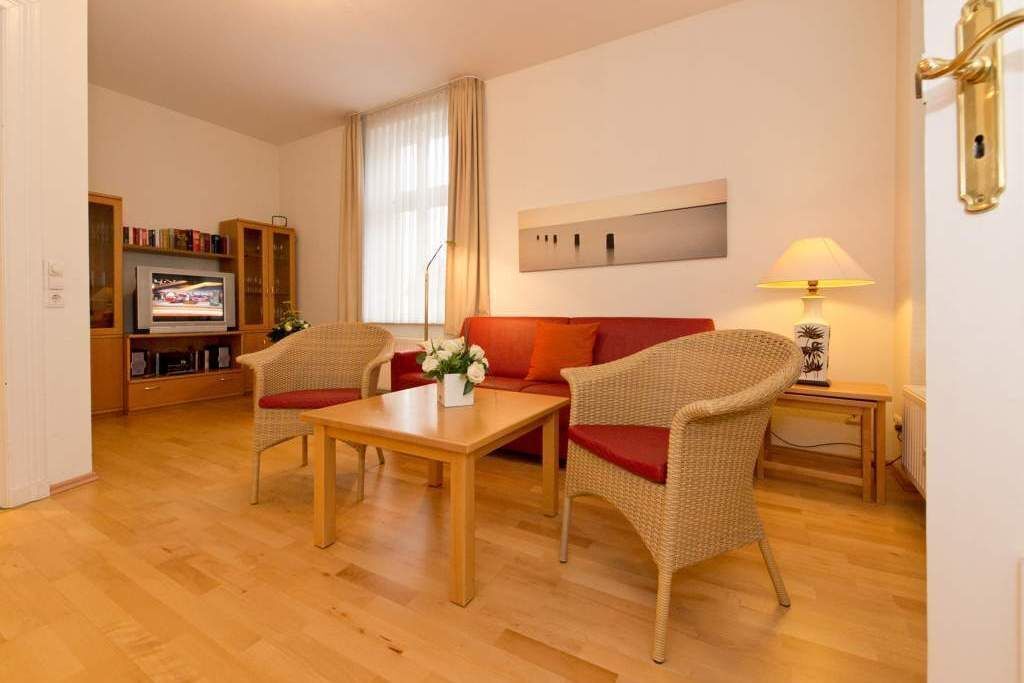 Un salon comprenant un canapé, deux fauteuils, une table basse en bois, un téléviseur et une bibliothèque.