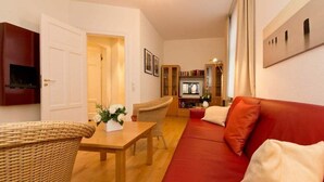 Un accogliente soggiorno con un divano rosso, una poltrona in vimini, un tavolino con un vaso e una televisione sullo sfondo.