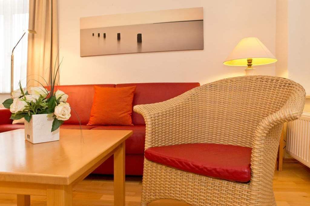A living room with a wicker chair, a red sofa, a wooden table, and a lamp.