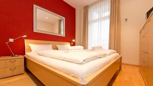 Un letto rifatto con lenzuola bianche, una lampada da comodino, un comodino in legno e uno specchio appeso al muro.