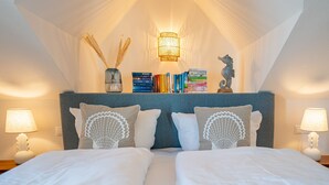 Een slaapkamer met een gewelfde plafond, een nachtkastje met een lamp, een boekenplank en decoratieve kussens.