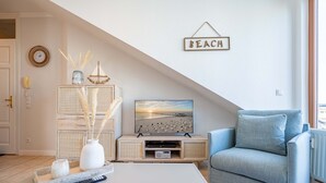 Een woonkamer met een televisie, een bank, een salontafel en een bord aan de muur waarop 'BEACH' staat.