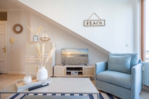 Olohuone, jossa on televisio, sohva, sohvapöytä ja seinälle kiinnitetty kyltti, jossa lukee ”BEACH”.