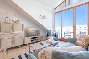 A modern living room with a television, sofa, and a balcony with a view.