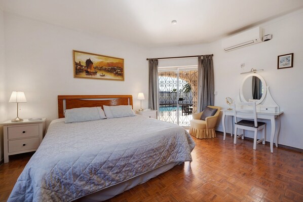 A bedroom with a bed, bedside tables, a desk with a chair, a window with curtains, and a painting on the wall.