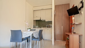 A compact kitchen with a dining table, chairs, a microwave, and a TV mounted on the wall.