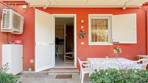 An open door leading to a kitchen, a dining table with chairs, and a small garden area with plants.