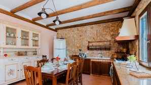 Une cuisine avec un mur en pierre, des armoires en bois, une table à manger pour quatre personnes et un four encastré.