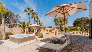 Une terrasse en pierre avec un jacuzzi, des chaises longues et des parasols.