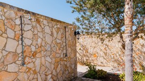 Un mur en pierre agrémenté d’un pommeau de douche en métal et d’un luminaire fixé au mur.