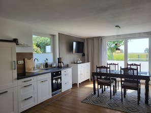 Eine moderne Küche mit weißen Schränken, einem eingebauten Backofen und einem Essbereich mit Tisch und Stühlen.