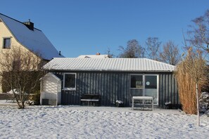 A house with a snow-covered roof, a small shed, and a bench in the yard.