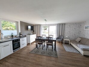 Una cocina moderna con armarios blancos, una zona de comedor con una mesa y sillas, un sofá y una alfombra estampada.