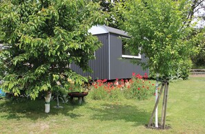 A building with a gray exterior, surrounded by green foliage and red flowers.