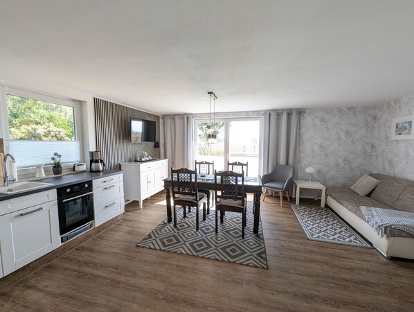 Une cuisine moderne avec des meubles blancs, un coin repas comprenant une table et des chaises, un canapé et un tapis à motifs.