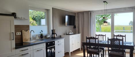 A modern kitchen with white cabinetry, a built-in oven, and a dining area with a table and chairs.