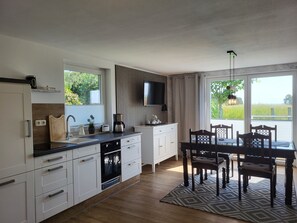 A modern kitchen with white cabinetry, a built-in oven, and a dining area with a table and chairs. - Cathrins Boddenblick - Cathrin`s Boddenblick (Wustrow)