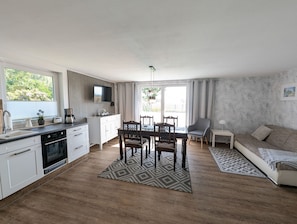 Eine moderne Küche mit weißen Schränken, ein Essbereich mit Tisch und Stühlen, ein Sofa und ein gemustertes Teppich.