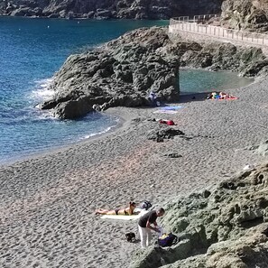 Une plage de galets avec une promenade en bois, une eau d’un bleu limpide et des gens qui prennent un bain de soleil.