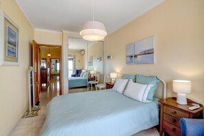 Une chambre d’hôtel avec un grand lit, des tables de chevet, une chaise, un miroir et une vue sur le couloir.