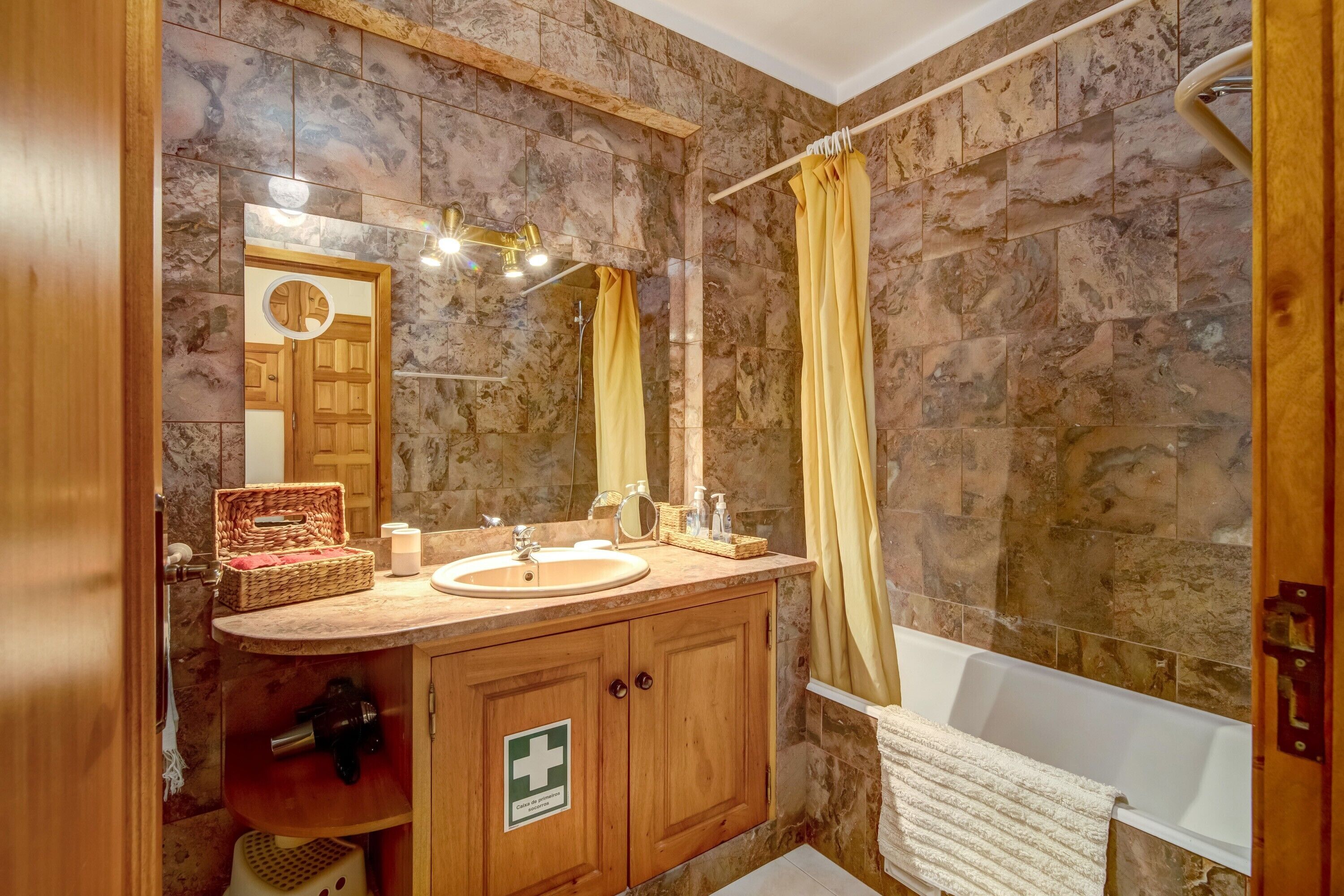 Une salle de bain avec un meuble-lavabo en bois, une baignoire, un rideau de douche et un miroir.