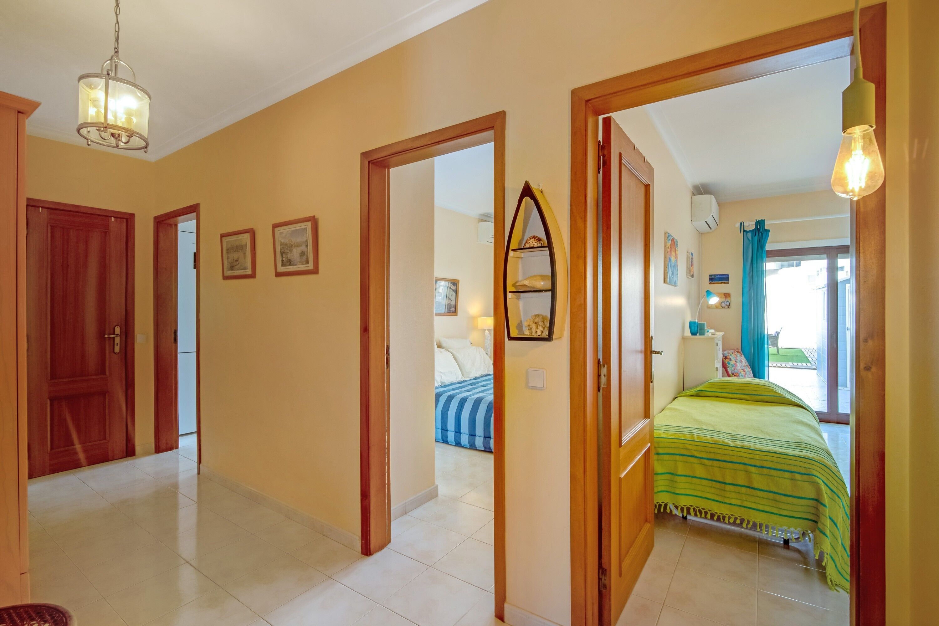 A hotel room with a bed, a wooden door, a mirror, and a hallway leading to another room.