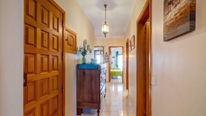 A hallway with wooden doors, a dresser, a hanging light fixture, and a bed in the distance. - Apartment 'Beira Mar' with Sea View, Terrace & Wi-Fi (Armação de Pêra)