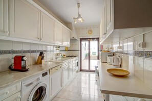 Une cuisine avec des meubles blancs, un lave-linge, un appareil électroménager rouge et un pare-feu en carrelage.