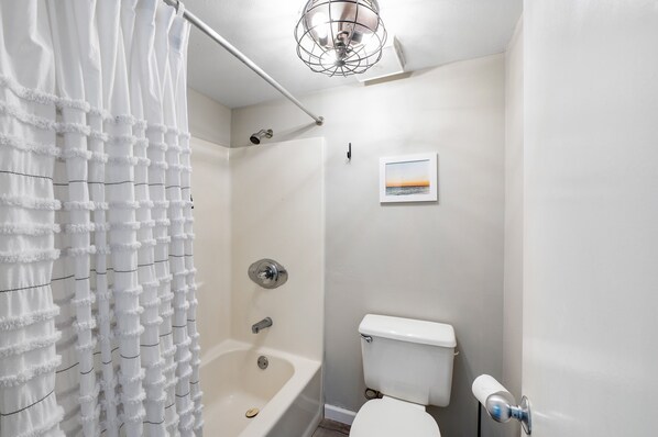 Un baño con cortina de ducha, bañera, inodoro y un cuadro en la pared.