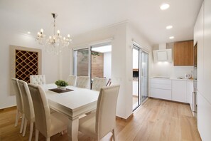 A modern kitchen with white cabinets, a built-in oven, and a dining area with a white table and chairs.