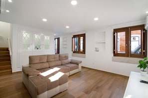 Un vaste espace de vie comprenant un canapé d’angle, un plancher en bois et un escalier menant à l’étage supérieur.