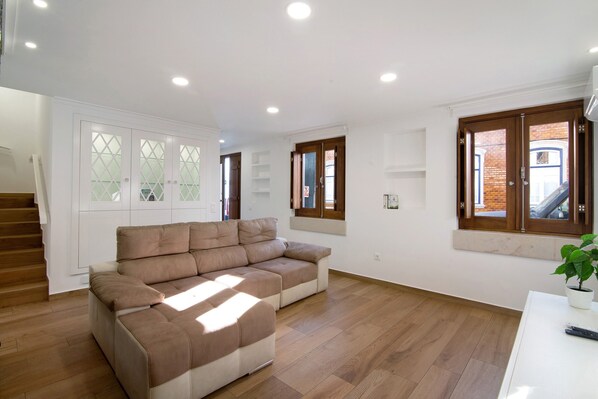 A spacious living area with a sectional sofa, wooden flooring, and a staircase leading to an upper floor.
