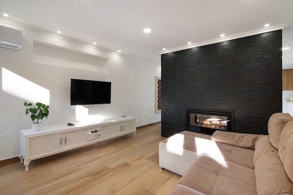 Un salon moderne doté d’un téléviseur à écran plat, d’une cheminée, d’un canapé beige et d’une console blanche.