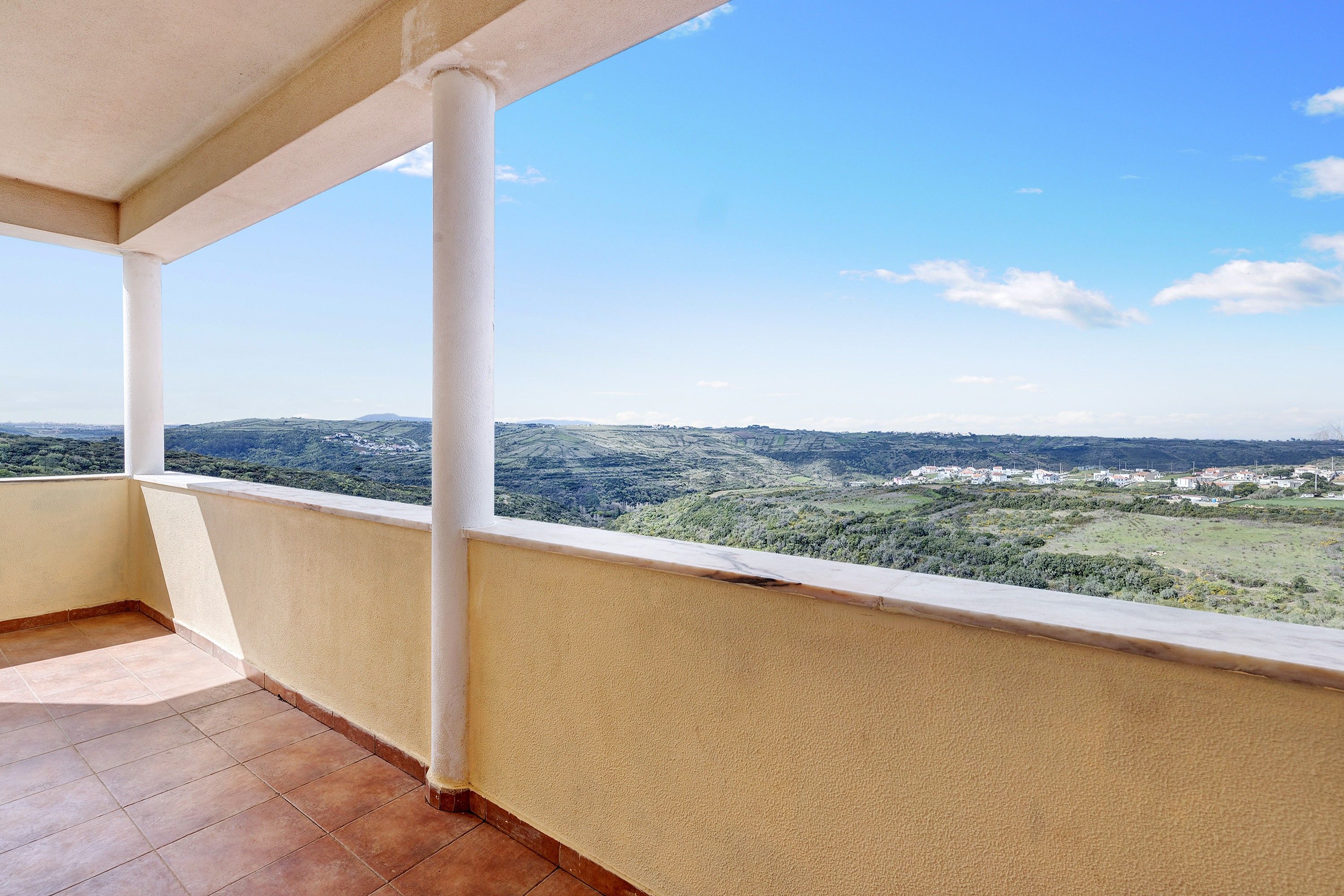Un balcon donnant sur un paysage vallonné et une ville située au loin.