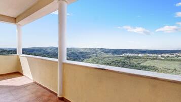 Un balcon donnant sur un paysage vallonné et une ville située au loin.