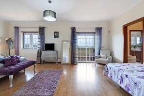 Una habitación amplia con sofá, cama, escritorio y silla. Cuenta con un ventanal grande y una puerta que da a un espacio exterior.