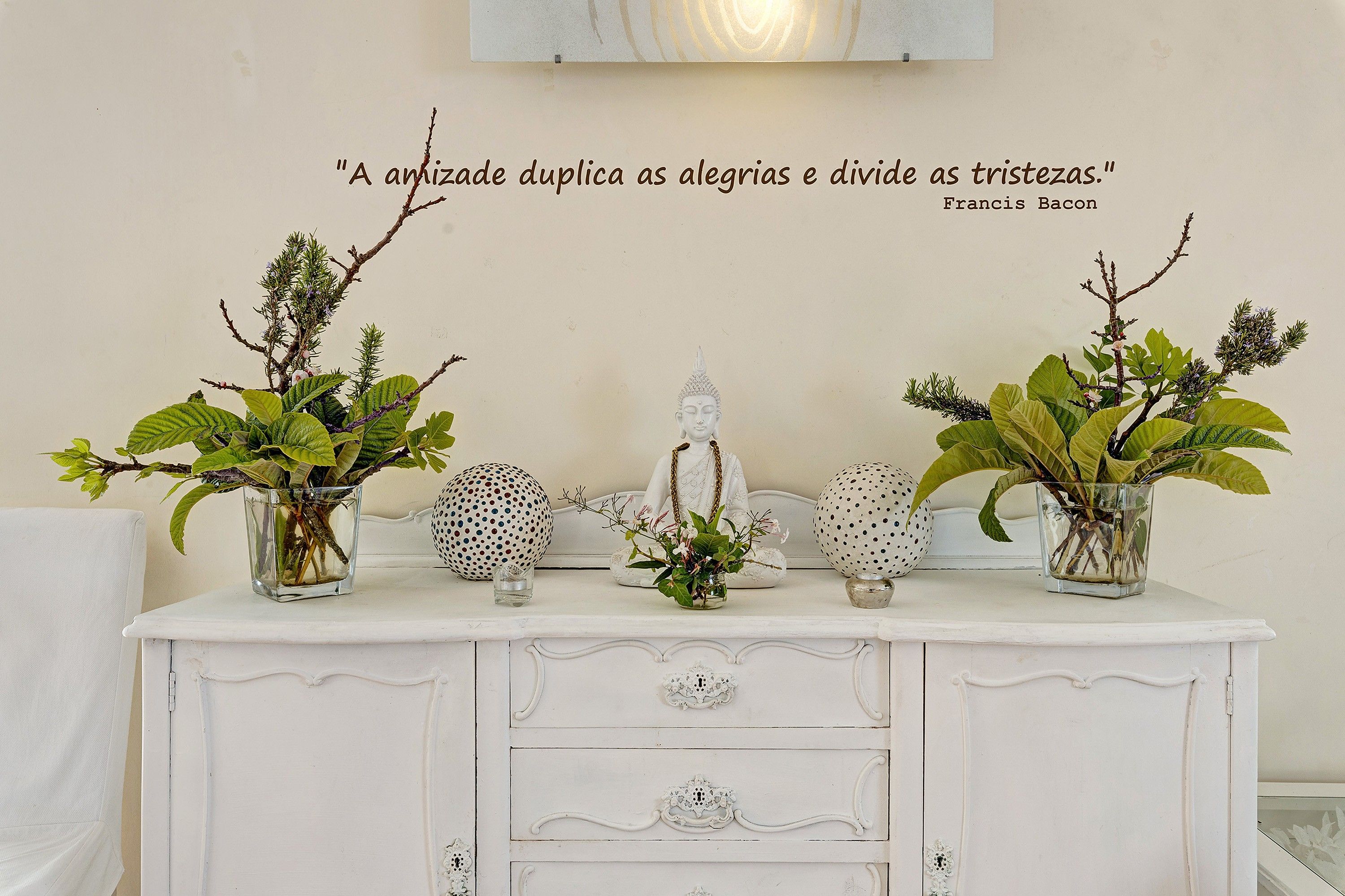 Une commode blanche agrémentée de vases décoratifs et d’une citation peinte sur le mur.