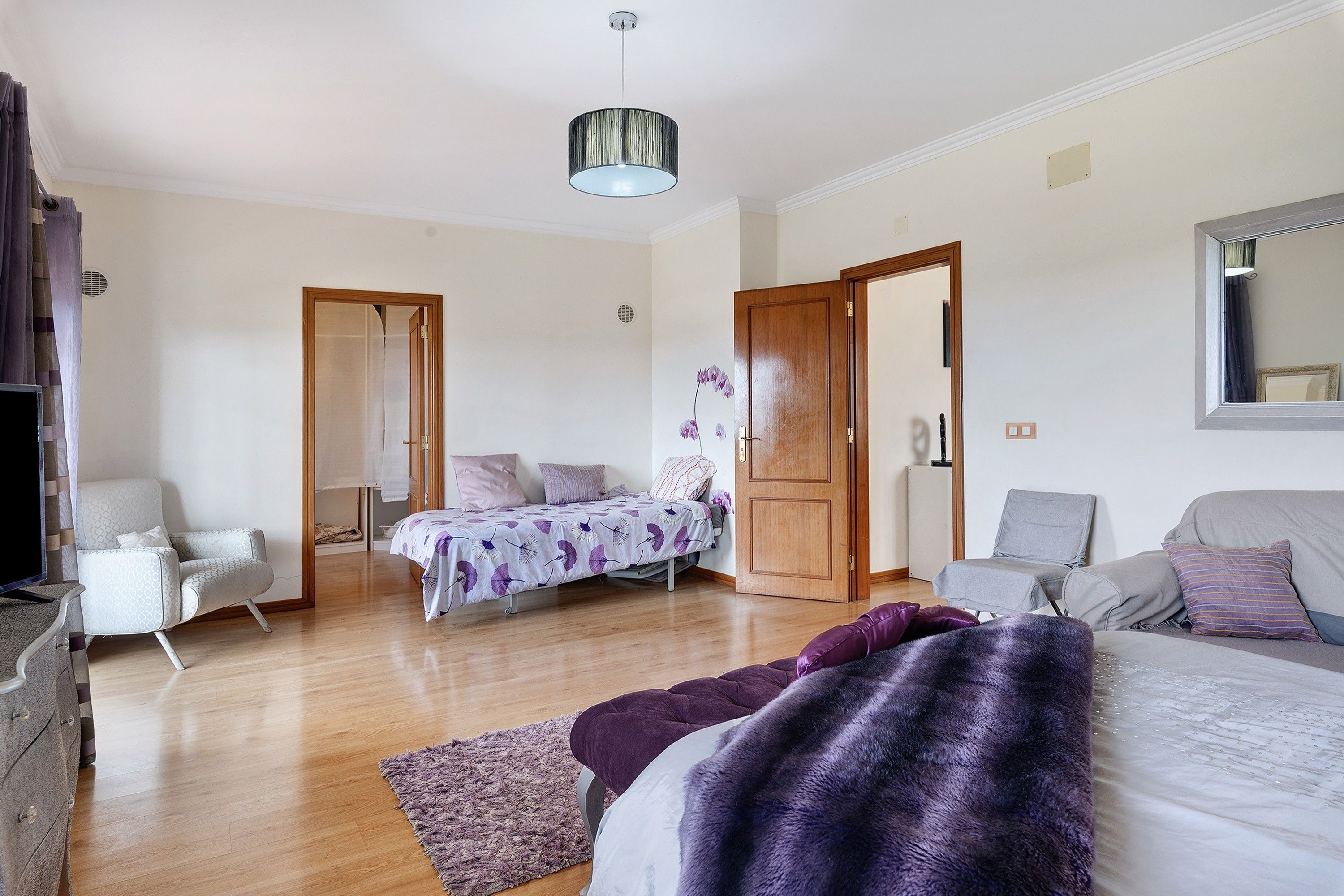 Une chambre à coucher avec un lit, une chaise, un canapé, un miroir et un luminaire au plafond.
