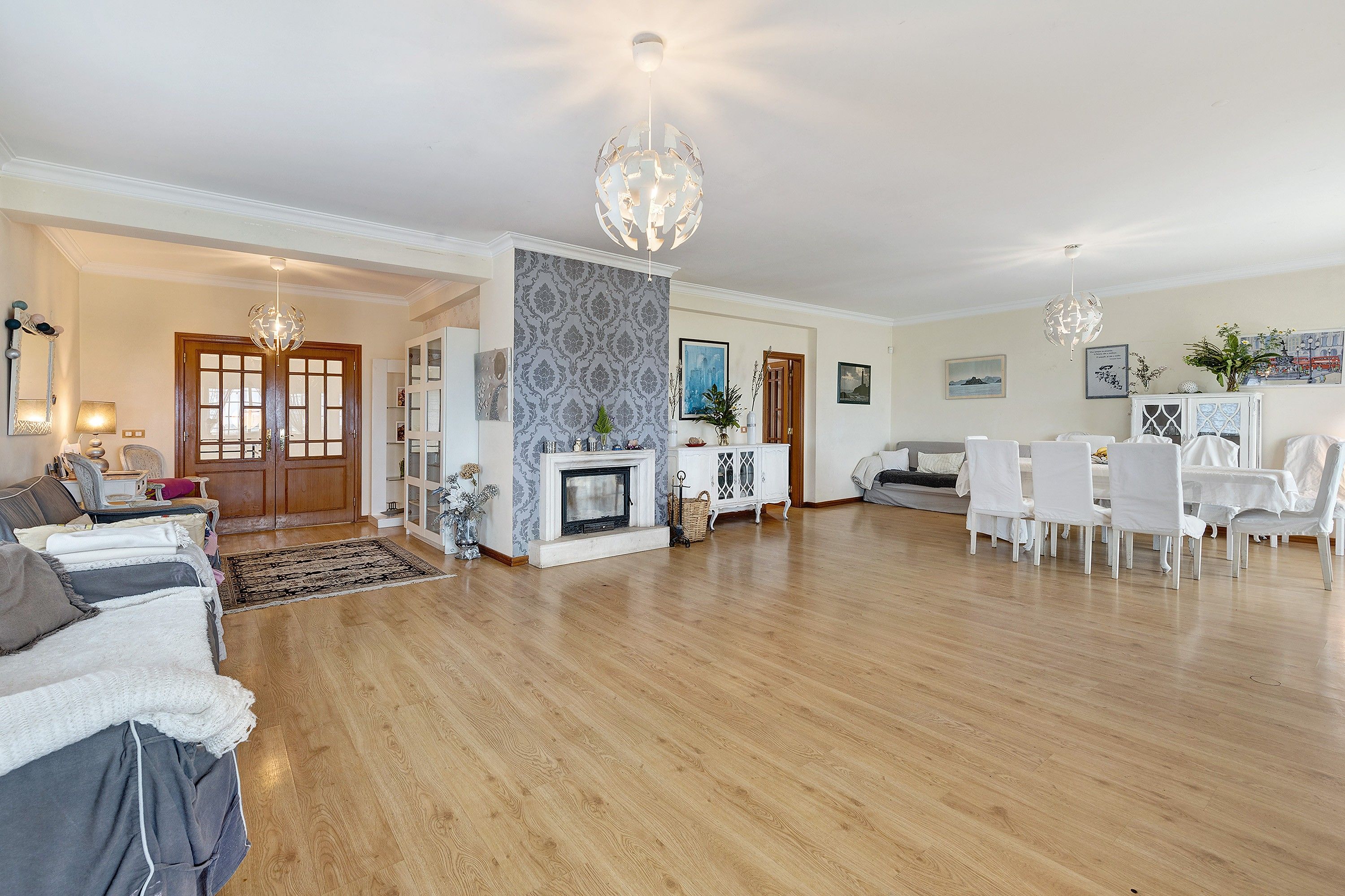 A spacious living room with a fireplace, wooden flooring, and a dining area with white chairs.