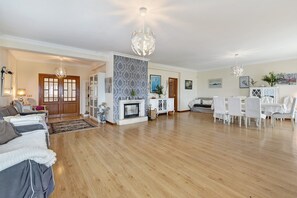 Amplia sala de estar con chimenea, piso de madera y un comedor con sillas blancas.