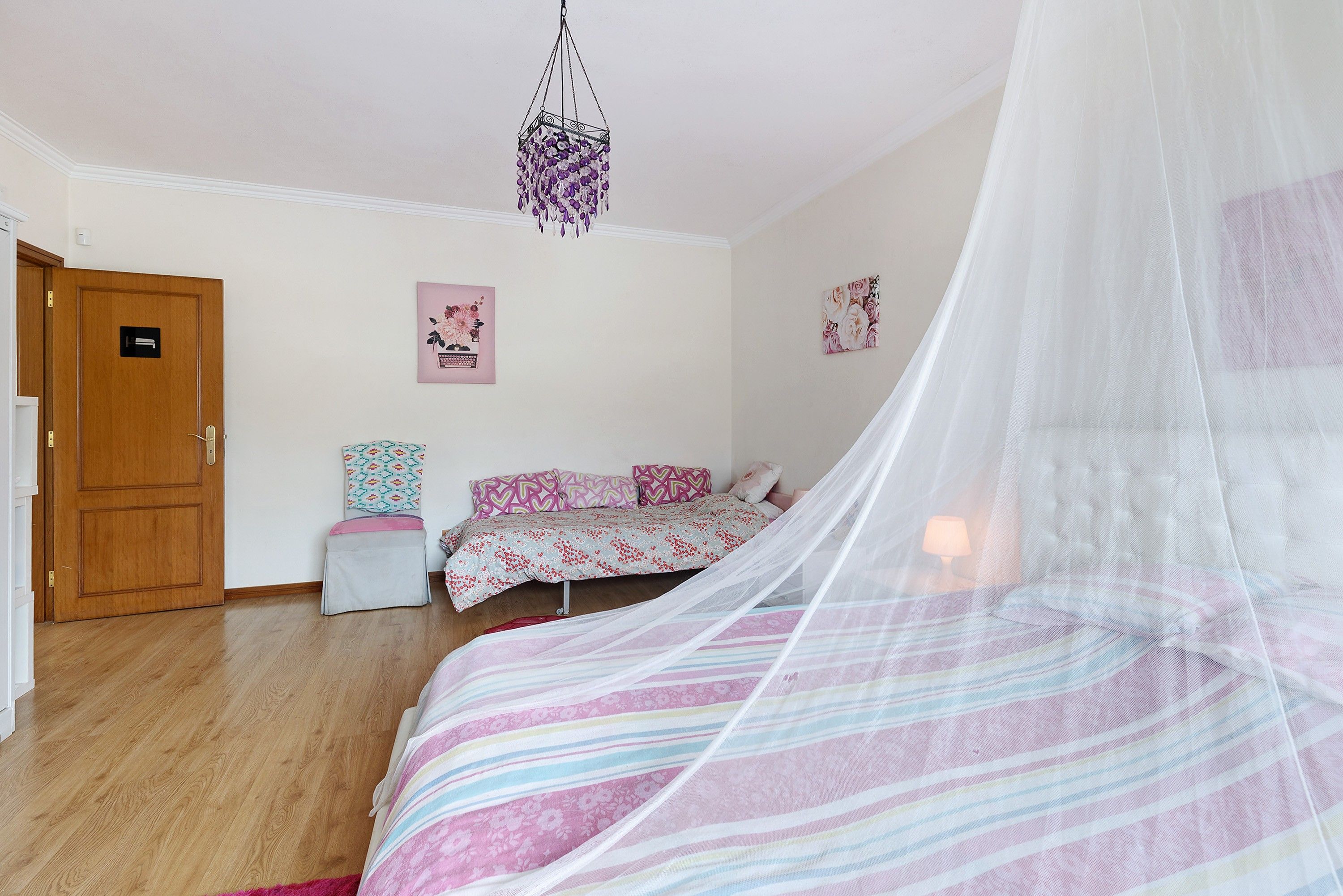 A bedroom with a bed, a bedside table, a chair, a door, and a hanging light fixture.