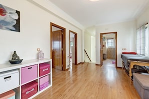 A hallway with wooden flooring, white walls, and a bed with a red pillow. There are pink storage bins and a small statue on a shelf.