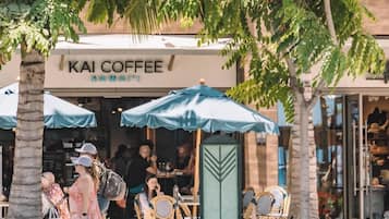 Una cafetería llamada 'KAI COFFEE' con terraza y palmeras.