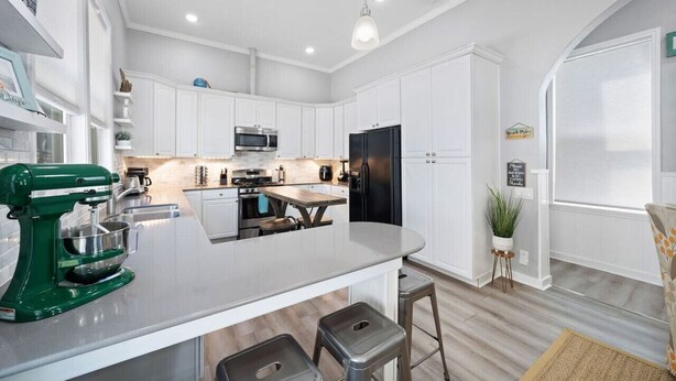 A modern kitchen with white cabinetry, a central island with stools, a green stand mixer, and a black refrigerator. - The Minted Mermaid - Pet Friendly - Winter Texan Rates! (Galveston)