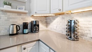 A kitchen with white cabinets, a coffee maker, a kettle, and a spice rack. - The Minted Mermaid - Pet Friendly - Winter Texan Rates! (Galveston)