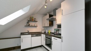 A kitchen with white cabinets, a stove, and a dishwasher. There is a skylight above the sink and a shelf with kitchen items.
