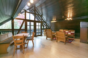 Een ruime kamer met een hoge plafond, houten balken, een grote eettafel met stoelen, een zithoek en een koelkast.