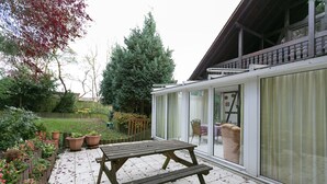 A patio with a wooden table and benches, surrounded by potted plants and a garden.